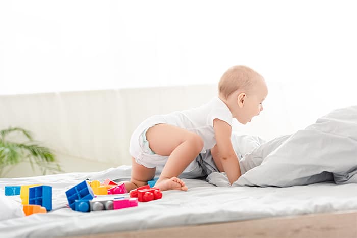 baby crawling on bed among toys